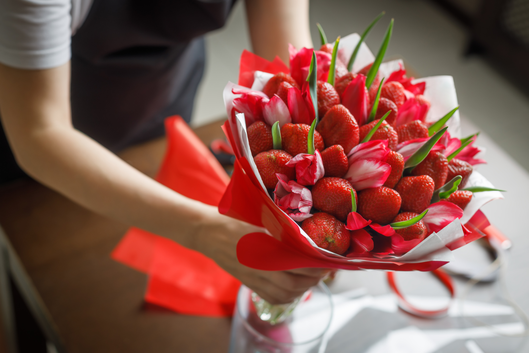 Woman in a black apron puts in a vase a beautiful original bouquet of tulips and strawberries
