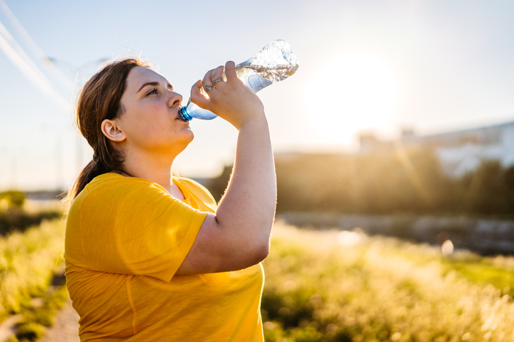 Oversized woman drinking water after running