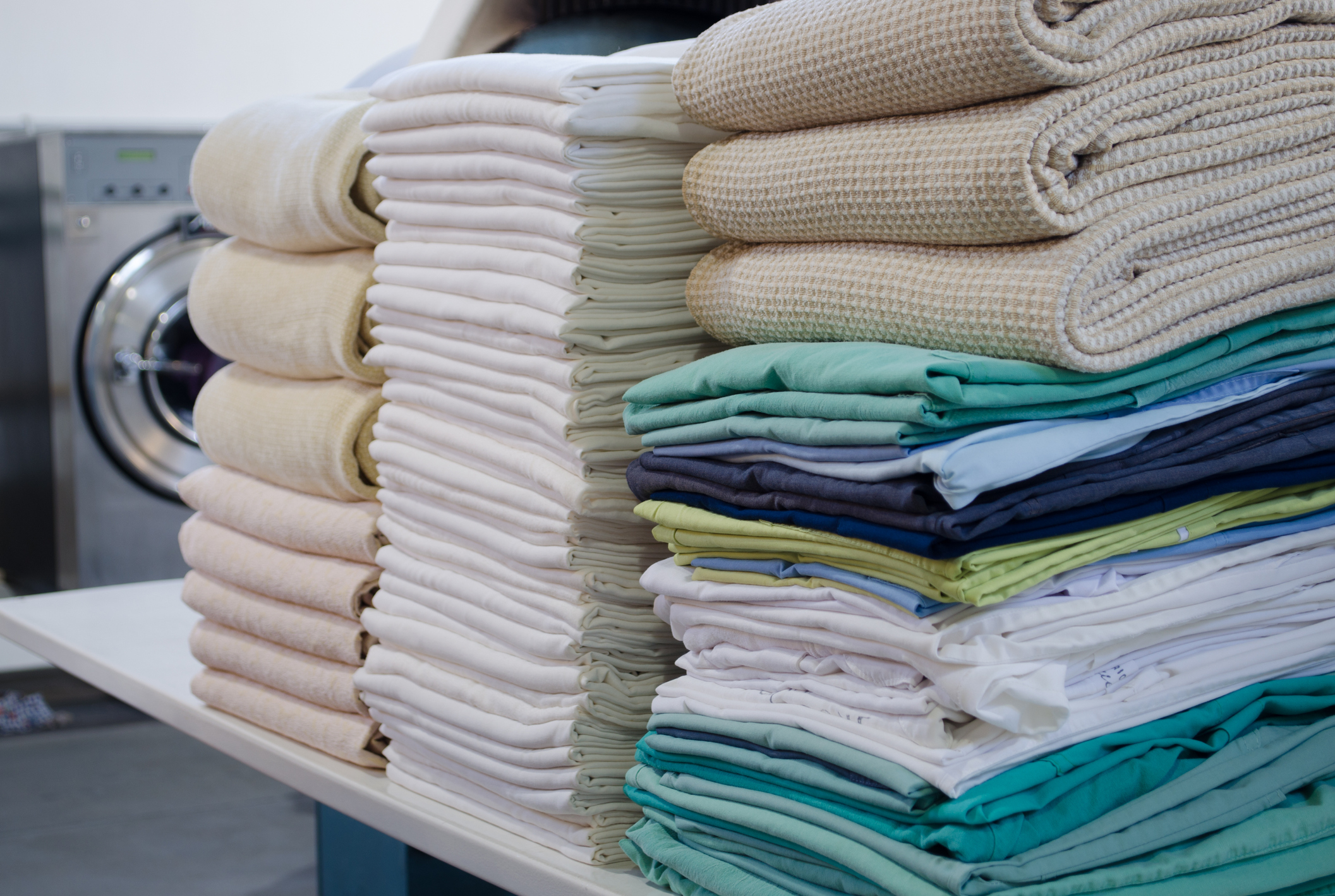 Stack of folded clean sheets, surgical clothes  and industrial iron in an industrial laundry. Cleaning and ironing service for hospitals and clinics. Selective focus.