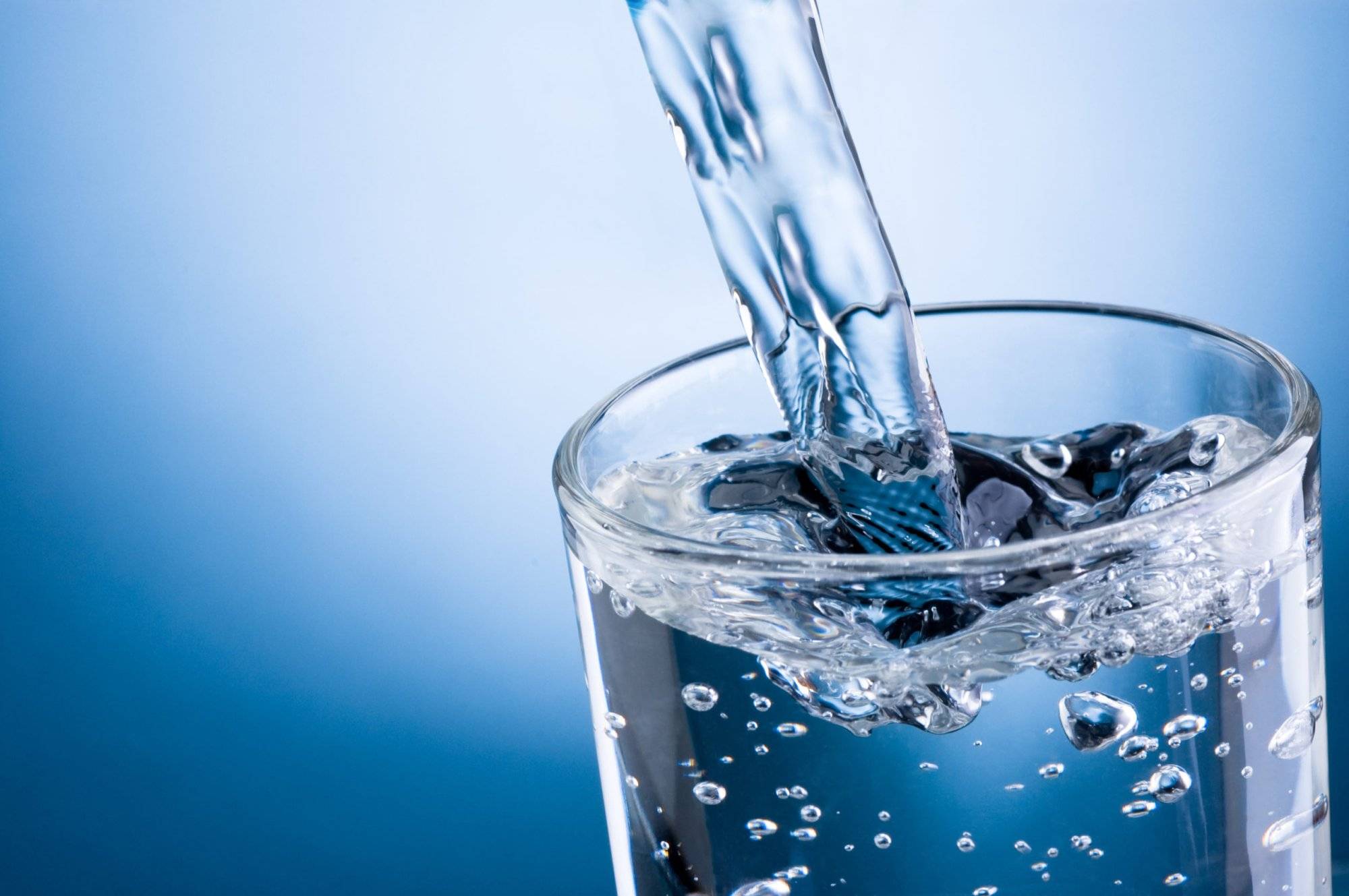 Pouring water into glass on blue background Pouring water into glass on blue background