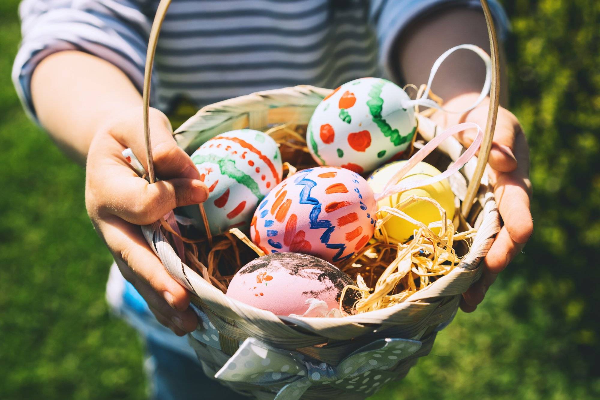 Colorful Easter eggs in basket. Children gathering painted decoration eggs in spring park. Kids hunt for egg outdoors.