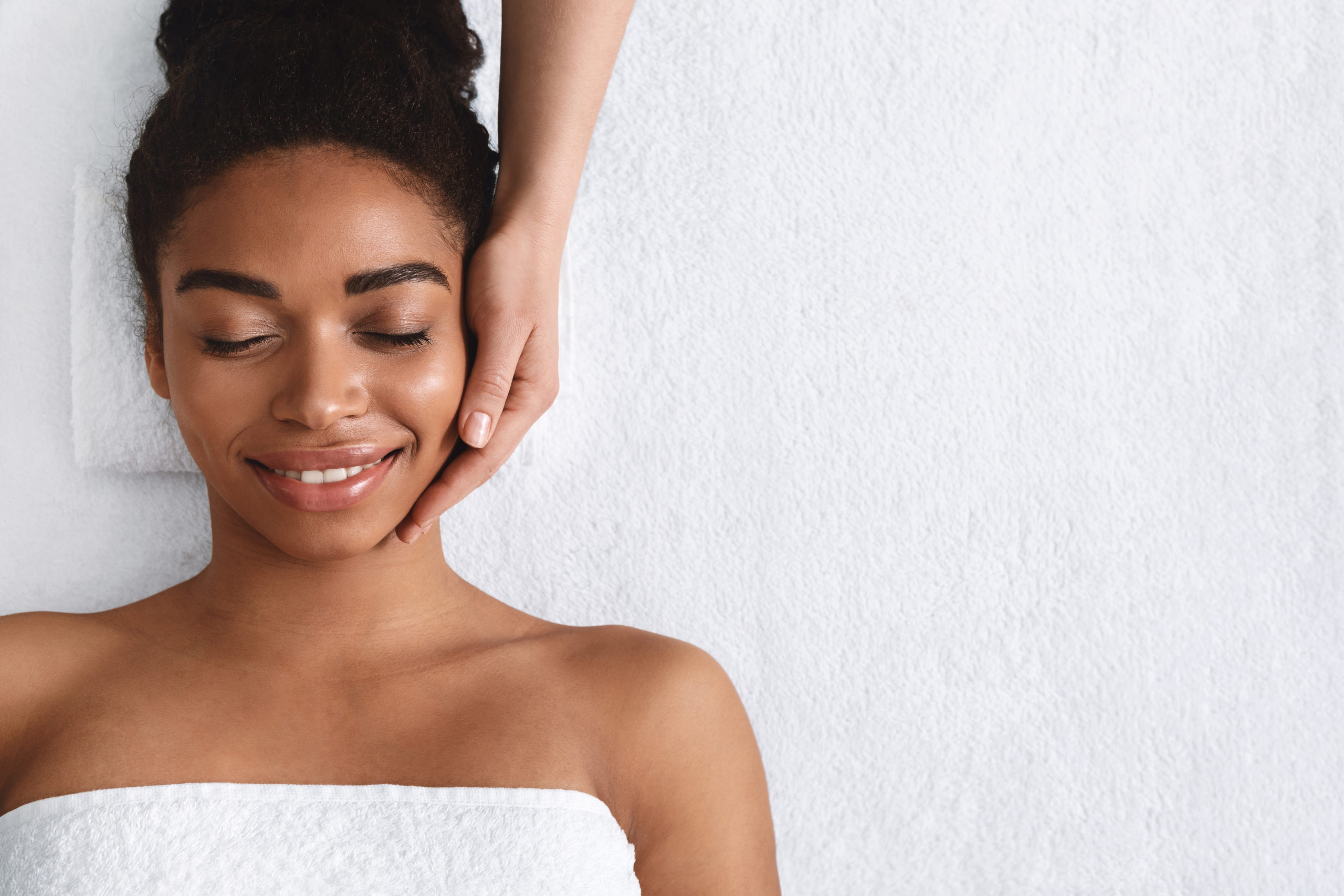 Joyful african girl having face massage at spa