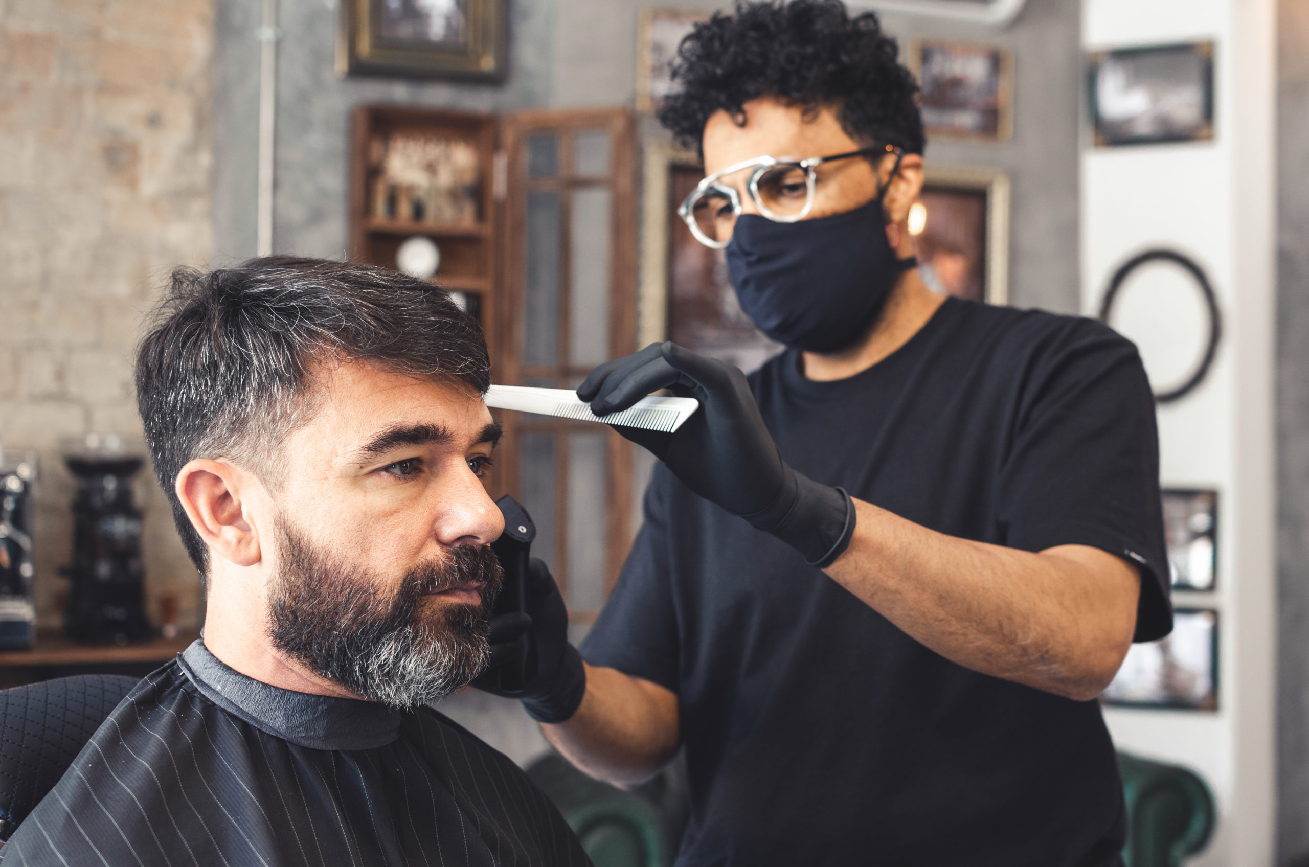 Mulatto hairdresser with mask and glasses combing a client