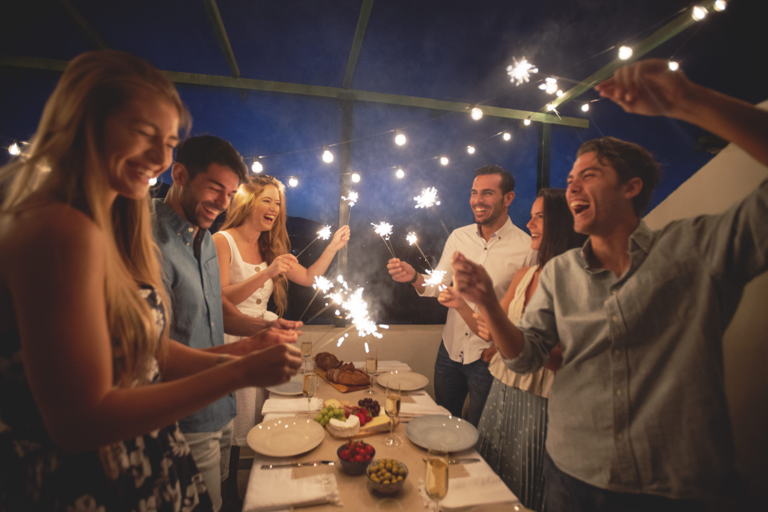 Group of friends holding sparklers and sharing a meal and a drink of champagne outdoors