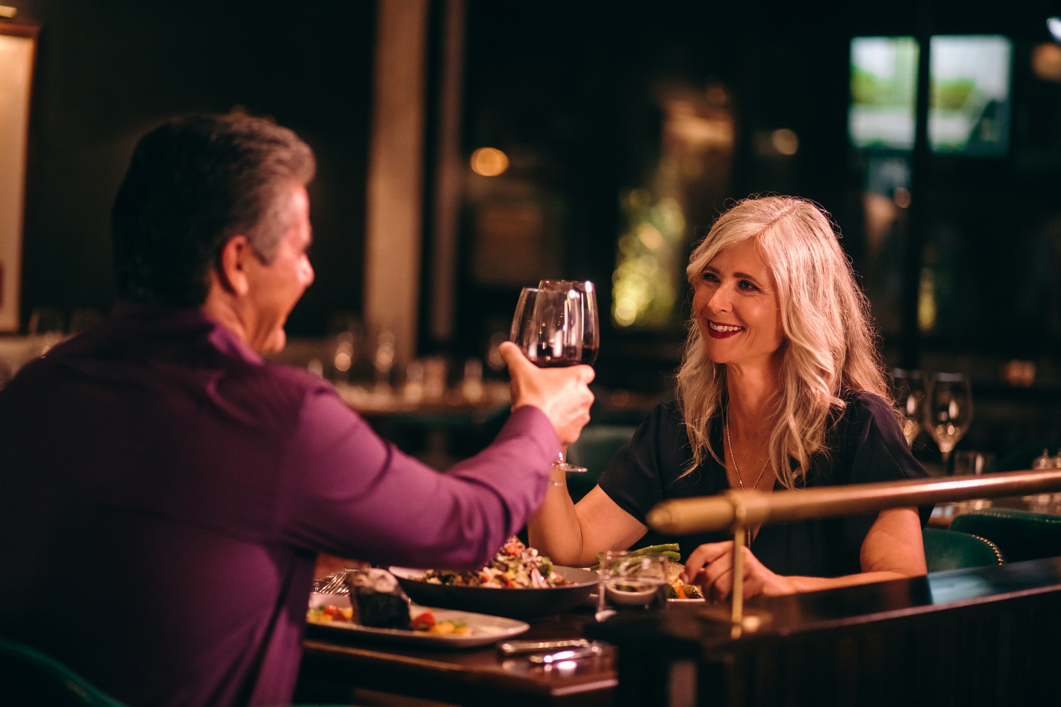 Smiling mature husband and wife toasting with wine at dinner